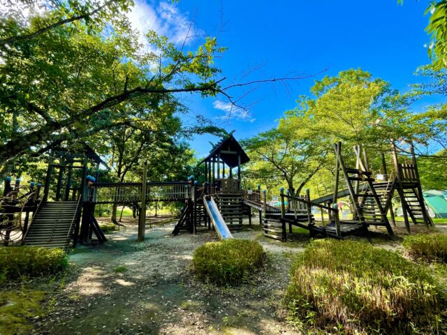 A large, wooden, multi-purpose adventure playground located in a park rich in natural beauty