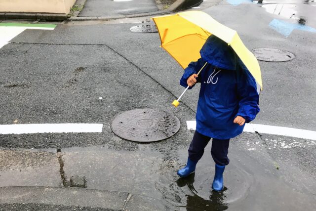 黄色い傘をさして雨の日に水たまりで遊ぶ子供