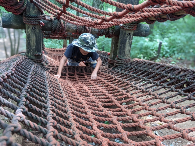 A child wearing a hat playing on the net course at Forest Adventure Tateshina