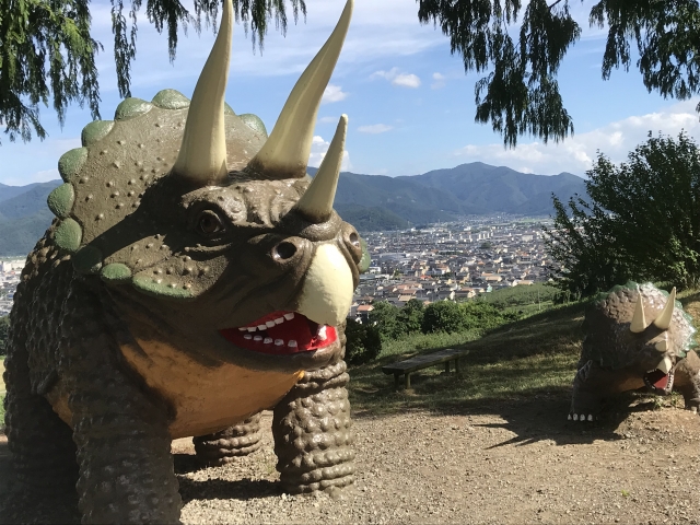 A large Triceratops monument installed on the grounds of Chausuyama Dinosaur Park and the cityscape of Nagano